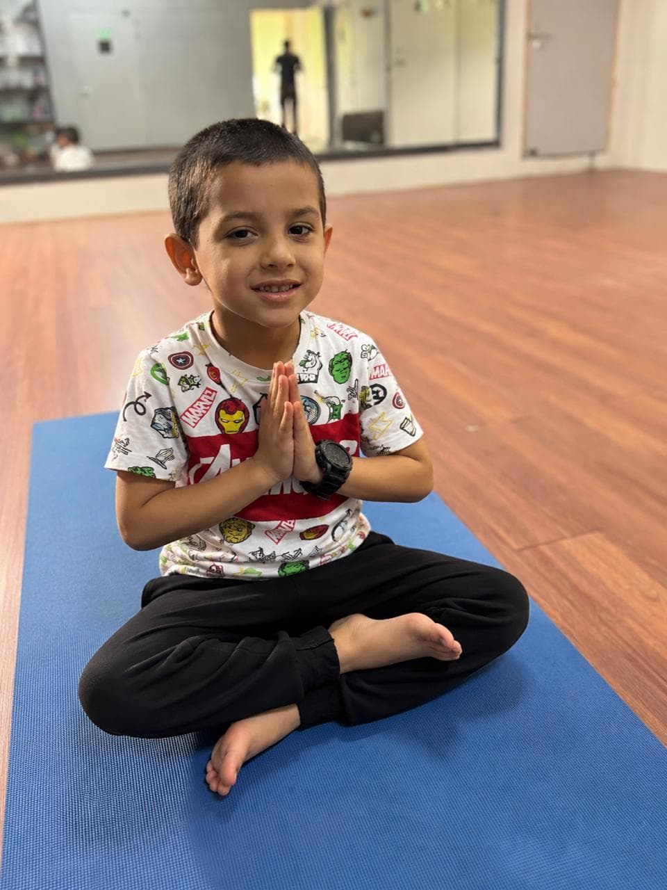 Child sitting in a calm yoga namaste pose on a mat